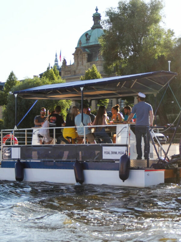A group of people are sitting, drinking and enjoying a sunny afternoon while cruising the Vltava river on a Prague beer boat.